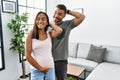 Young interracial couple expecting a baby, touching pregnant belly smiling confident touching hair with hand up gesture, posing Royalty Free Stock Photo