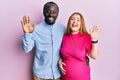 Young interracial couple expecting a baby, touching pregnant belly waiving saying hello happy and smiling, friendly welcome Royalty Free Stock Photo