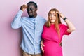 Young interracial couple expecting a baby, touching pregnant belly worried and stressed about a problem with hand on forehead,