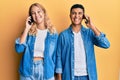 Young interracial couple having conversation talking on the smartphone looking positive and happy standing and smiling with a Royalty Free Stock Photo