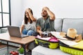 Young interracial couple packing summer clothes in suitcase looking at laptop stressed and frustrated with hand on head, surprised Royalty Free Stock Photo