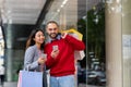 Young interracial couple with smartphones standing on street with shopper bags, buying goods online near big city mall Royalty Free Stock Photo