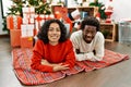 Young interracial couple smiling happy lying on the floor by christmas tree at home Royalty Free Stock Photo