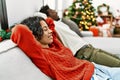 Young interracial couple smiling happy relaxing with hands on head sitting on the sofa by christmas tree at home Royalty Free Stock Photo