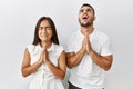 Young interracial couple standing together in love over isolated background begging and praying with hands together with hope Royalty Free Stock Photo