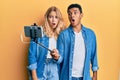 Young interracial couple taking a selfie photo with smartphone afraid and shocked with surprise and amazed expression, fear and