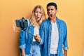 Young interracial couple taking a selfie photo with smartphone angry and mad screaming frustrated and furious, shouting with anger