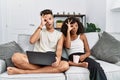 Young interracial couple using laptop at home sitting on the sofa doing ok gesture shocked with surprised face, eye looking Royalty Free Stock Photo