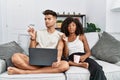 Young interracial couple using laptop at home sitting on the sofa pointing aside worried and nervous with forefinger, concerned Royalty Free Stock Photo