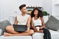 Young interracial couple using laptop at home sitting on the sofa smiling looking to the side and staring away thinking Royalty Free Stock Photo
