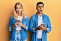 Young interracial couple using smartphone in shock face, looking skeptical and sarcastic, surprised with open mouth Royalty Free Stock Photo