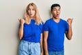 Young interracial couple wearing casual clothes surprised pointing with hand finger to the side, open mouth amazed expression Royalty Free Stock Photo