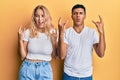Young interracial couple wearing casual white tshirt shouting with crazy expression doing rock symbol with hands up Royalty Free Stock Photo