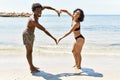 Young interracial tourist couple wearing swimwear doing big heart with arms at the beach