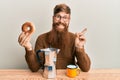 Young irish redhead man sitting on the table having breakfast smiling happy pointing with hand and finger to the side