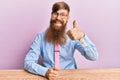 Young irish redhead man wearing business shirt and tie sitting on the table doing happy thumbs up gesture with hand Royalty Free Stock Photo