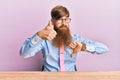 Young irish redhead man wearing business shirt and tie sitting on the table doing thumbs up and down, disagreement and agreement Royalty Free Stock Photo