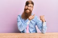 Young irish redhead man wearing business shirt and tie sitting on the table pointing to the back behind with hand and thumbs up, Royalty Free Stock Photo