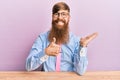 Young irish redhead man wearing business shirt and tie sitting on the table showing palm hand and doing ok gesture with thumbs up, Royalty Free Stock Photo