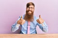 Young irish redhead man wearing business shirt and tie sitting on the table success sign doing positive gesture with hand, thumbs Royalty Free Stock Photo