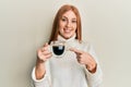 Young irish woman drinking a cup of coffee smiling happy pointing with hand and finger