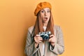 Young irish woman holding vintage camera afraid and shocked with surprise and amazed expression, fear and excited face Royalty Free Stock Photo