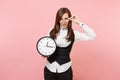 Young irritated dissatisfied business woman in black suit, glasses holding alarm clock on pastel pink Royalty Free Stock Photo