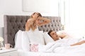 Young irritated woman sitting in bed with pillows at home. Problem with snoring