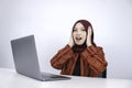 Young Asian Islam woman wearing headscarf is shocked and excited with what she see on laptop on the table