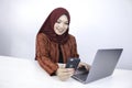 Young Islam woman wearing headscarf is smiling on a mobile phone with laptop on the table