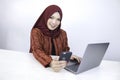 Young Islam woman wearing headscarf is smiling on a mobile phone with laptop on the table