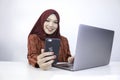 Young Islam woman wearing headscarf is smiling on a mobile phone with laptop on the table