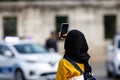 Young Islamic woman taking photos on phone, back view. Shooting video with cell phone camera, using smartphone to take pictures Royalty Free Stock Photo