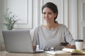 Young Italian female freelancer holding credit card, using laptop while making payments online