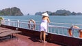 Young Italian woman in white dress and traditional Vietnamese conical rice hat standing on an upper deck of a cruise ship