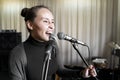 Young Japanese or Caucasian woman singing song loud on two microphones in studio