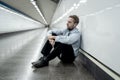 Young jobless business man suffering depression sitting on ground street underground leaning on wall alone looking desperate in