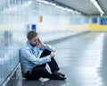 Young jobless business man suffering depression sitting on ground street underground leaning on wall alone looking desperate in Royalty Free Stock Photo