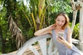 Young jocund woman using smartphone with palms in background, sitting on swing. Royalty Free Stock Photo