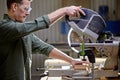 Young joiner making woodcraft furniture in wood workshop using electric machine