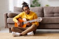 Young joyful african american man playing acoustic guitar at home, sitting on floor in living room Royalty Free Stock Photo