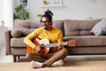 Young joyful african american man playing acoustic guitar at home, sitting on floor in living room Royalty Free Stock Photo