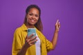 Young joyful African American woman with phone points finger at copy space Royalty Free Stock Photo