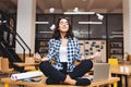 Young joyful brunette woman having meditation on table surround work stuff and flying papers. Cheerful mood, taking a Royalty Free Stock Photo