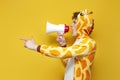 young joyful guy in funny children\'s giraffe pajamas speaks into megaphone and points his hand to the side