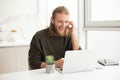 Young joyful man in earphones sitting at the table and laughing while looking in laptop at home Royalty Free Stock Photo