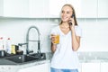 Young joyful woman drinking orange juice while talking mobile phone and standing near a kitchen table Royalty Free Stock Photo