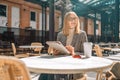 Blonde female freelancer working in a street cafe uses a tablet outdoor at cozy cafe terrace. Royalty Free Stock Photo