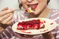 Young joyful woman is tasting a piece of cheesecake with raspberries, sweet food Royalty Free Stock Photo