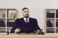 Young judge in a gown sitting at his table in the courtroom and reading the sentence Royalty Free Stock Photo